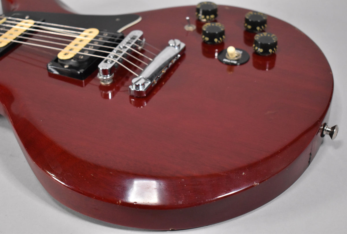 Close-up of the cherry-finished body, showing the bridge, two pickups with cream bobbins, four black control knobs, and a few dings.