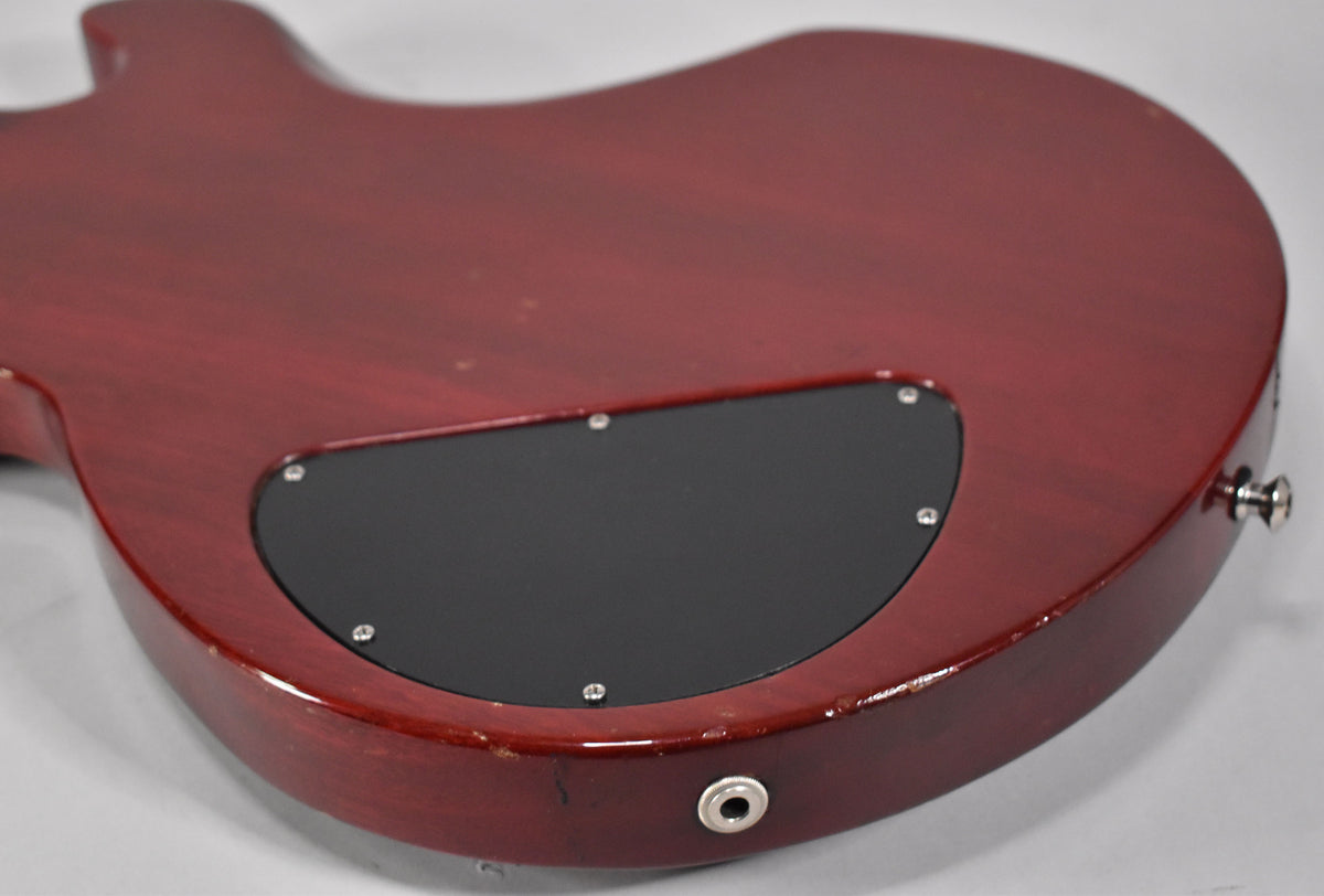 The guitar's cherry red back shows a black control cavity cover, output jack, and strap button, with visible wear along the edges.