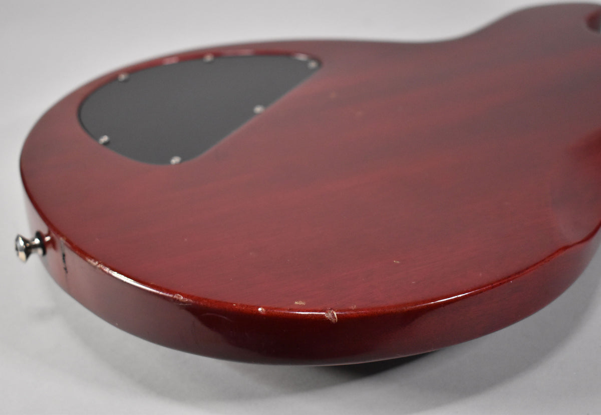 The back of the cherry red guitar body, showing a black control cavity cover and several chips and dings along the lower edge.