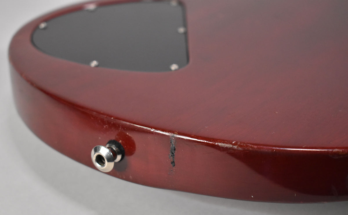 Close-up of the guitar's lower bout, showing the cherry finish, input jack, and a deep scratch with surrounding wear on the edge.