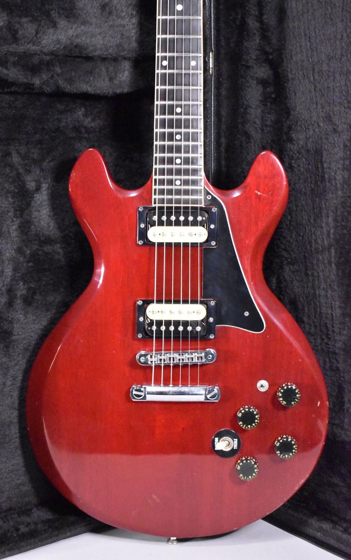 Full-frame view of a cherry-red guitar with a glossy finish, showing two humbuckers, a black pickguard, and four black control knobs.