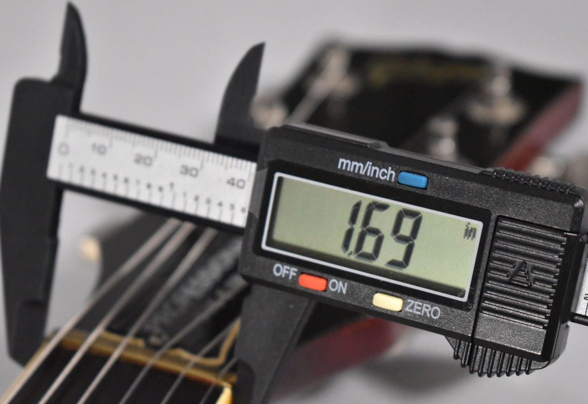 Digital calipers measure the guitar's nut width at 1.69 inches, with the headstock and tuning pegs blurred in the background.