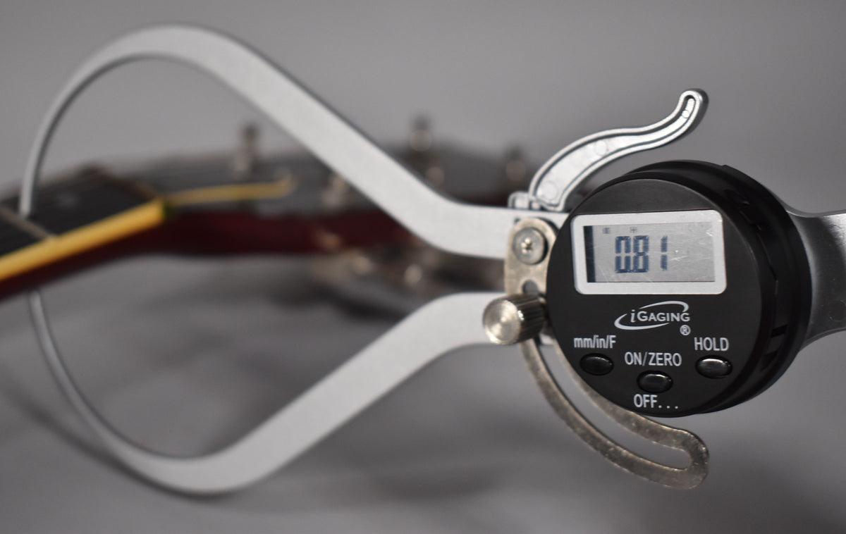 A digital caliper measuring a guitar neck, displaying "0.81" on its screen.