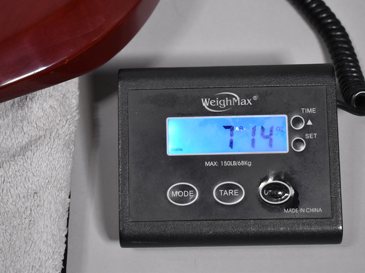Close-up of a digital scale displaying "7 LB 14 OZ", with the guitar's cherry finish body resting on a white cloth to the left.