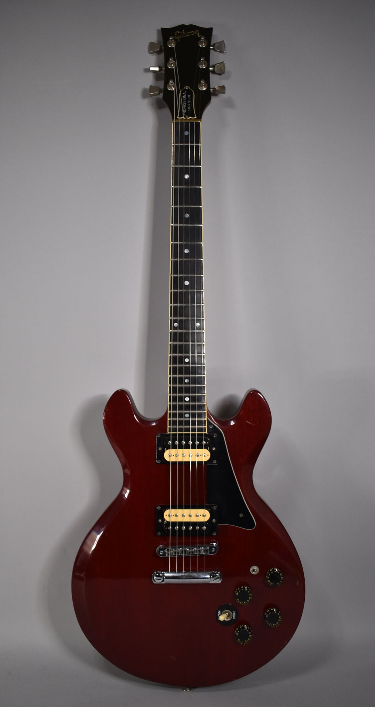 Full-length, front view of a cherry-finished electric guitar with gold humbuckers, black pickguard, and four black control knobs.
