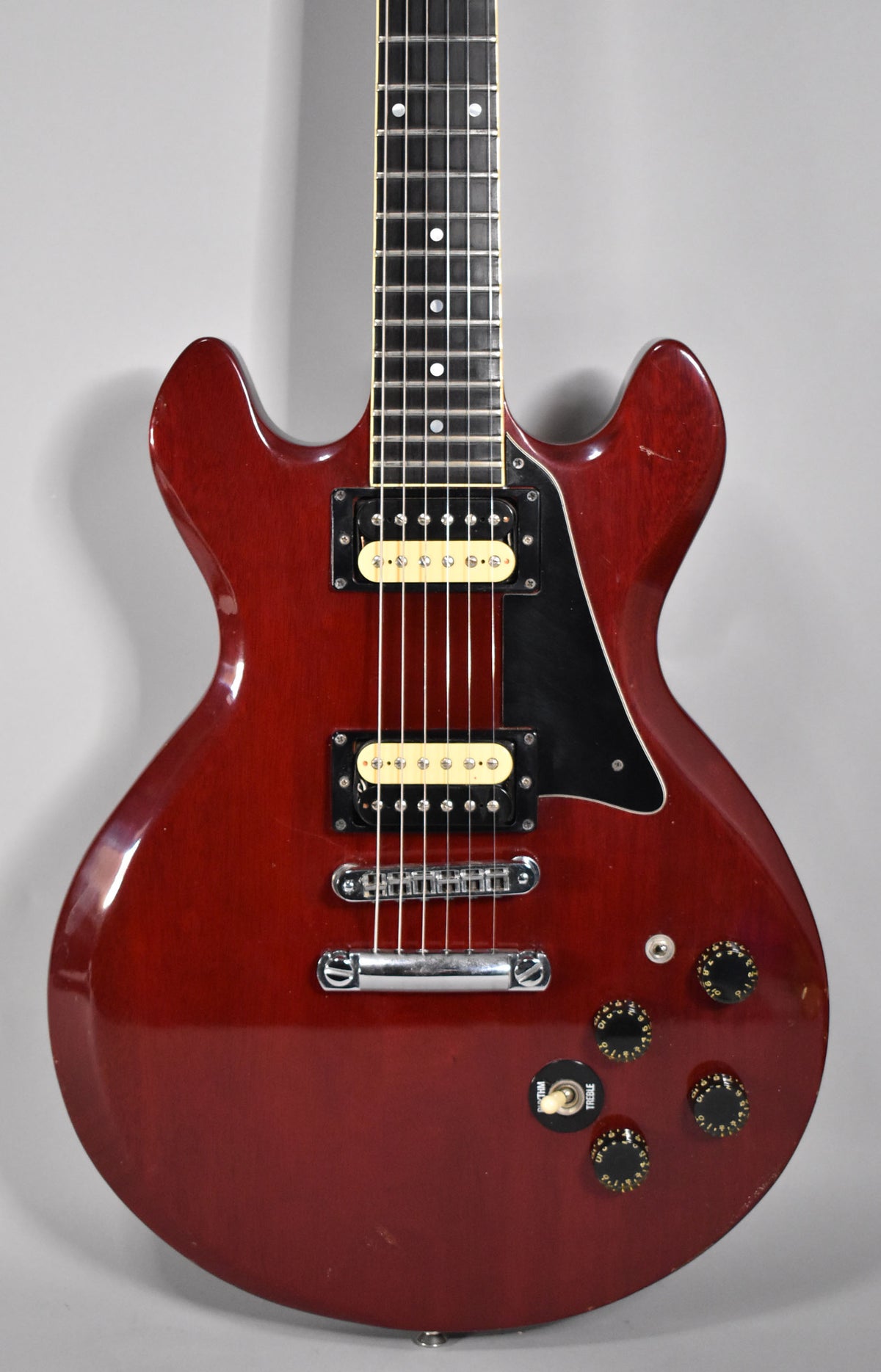 Full-frame view of a cherry red electric guitar with two cream humbuckers, a black pickguard, and four black control knobs.