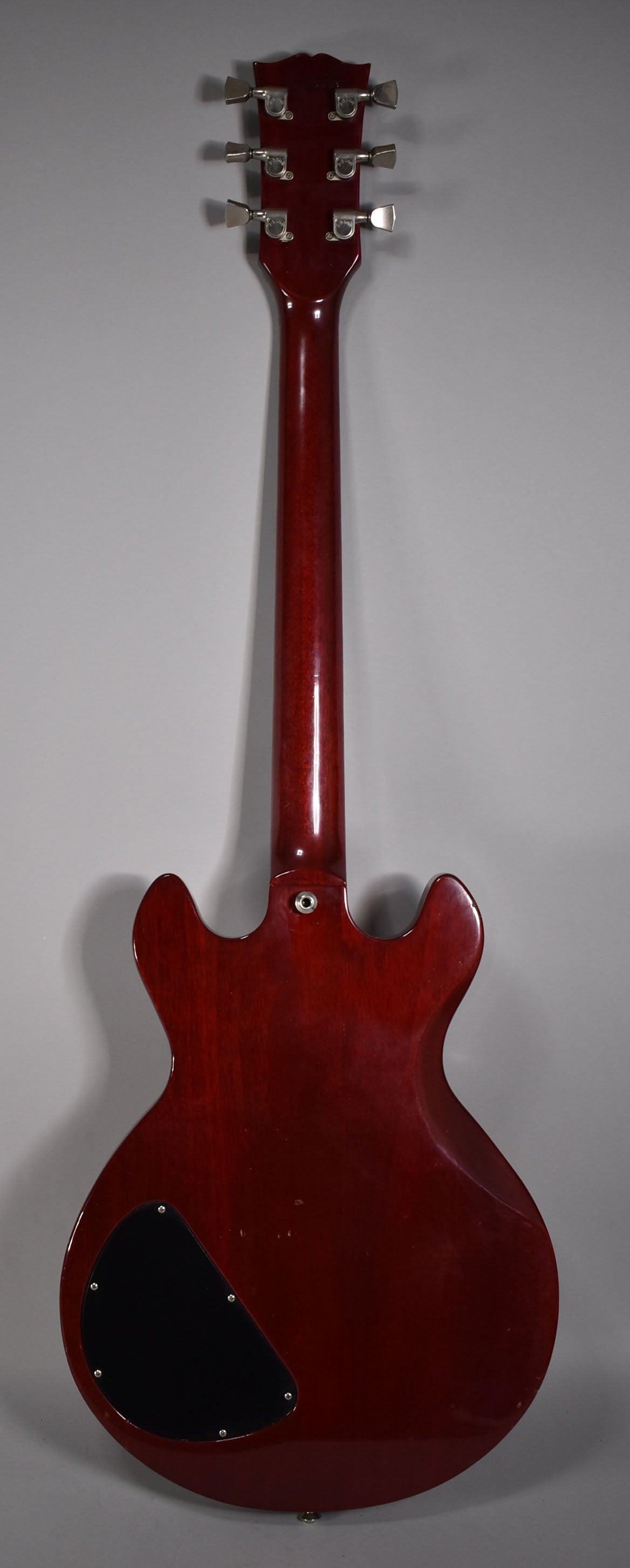 The full back of a cherry red guitar with a glossy finish, showing six chrome tuners and a black control cavity cover.