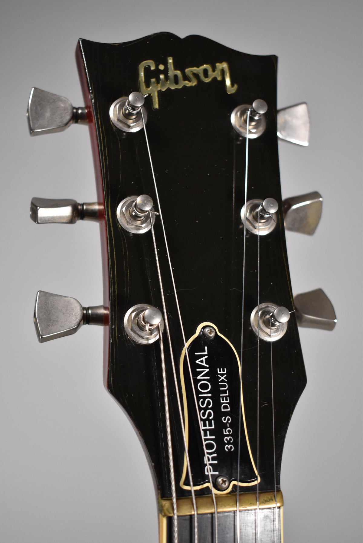 Close-up of the black headstock with six chrome tuners, showing finish checking and a bell-shaped truss rod cover.