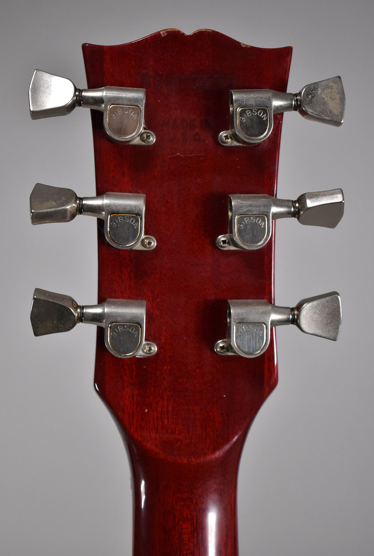 The back of a cherry red headstock with six chrome tuners, showing some finish wear along the top edge.