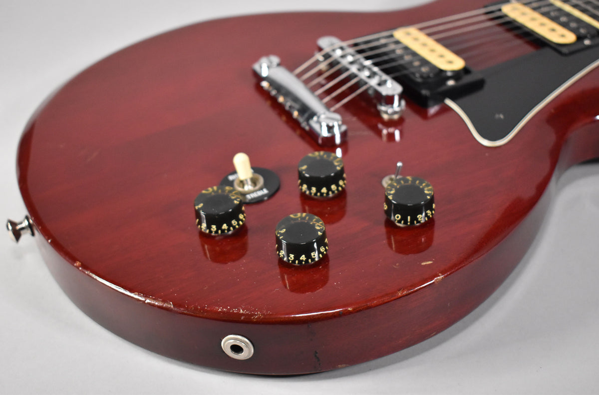 Close-up of the cherry-finished body, showing four black numbered control knobs, a cream toggle switch, and a chrome output jack.