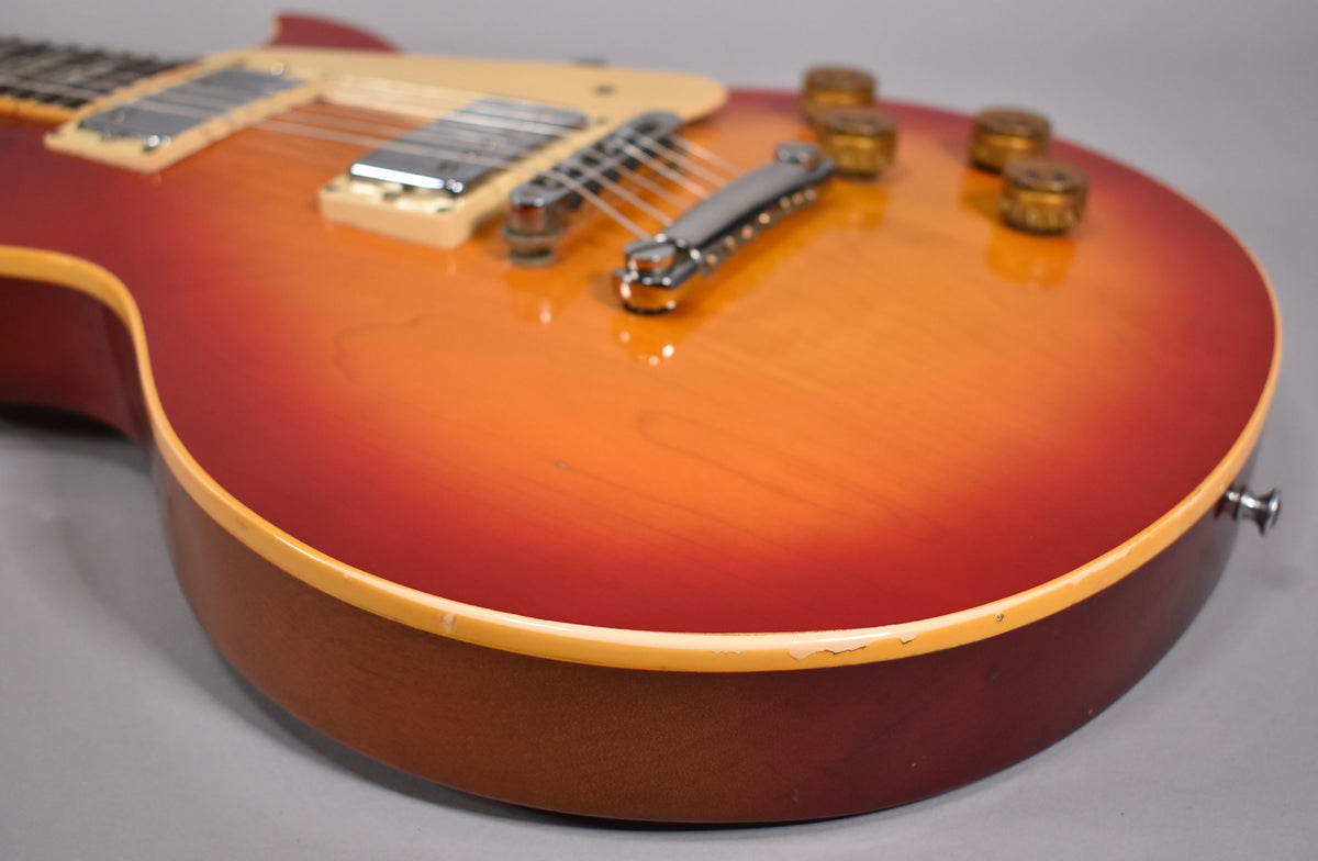 Close-up of the guitar body, showing the cherry sunburst finish, cream binding with chips, chrome hardware, and four gold control knobs.