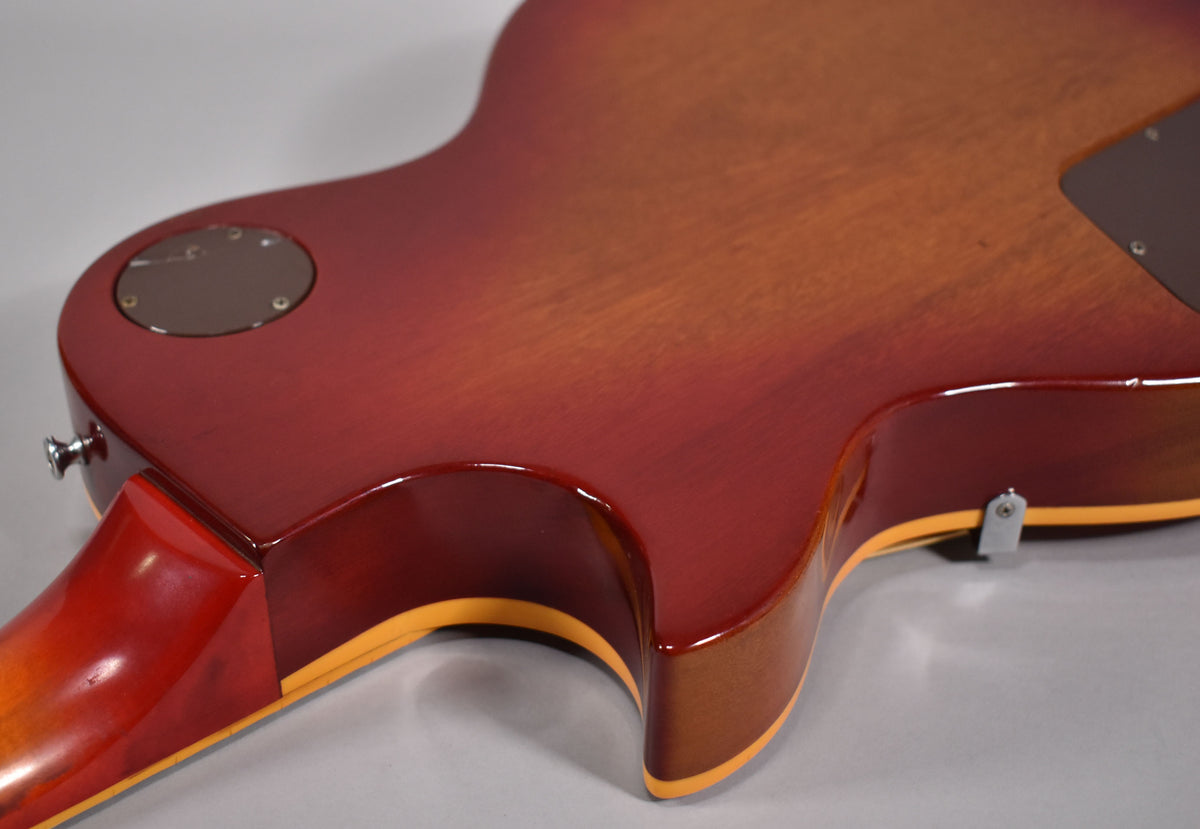The guitar's cherry sunburst back shows a strap button, control cavity cover, and a small metal bracket near the lower bout.