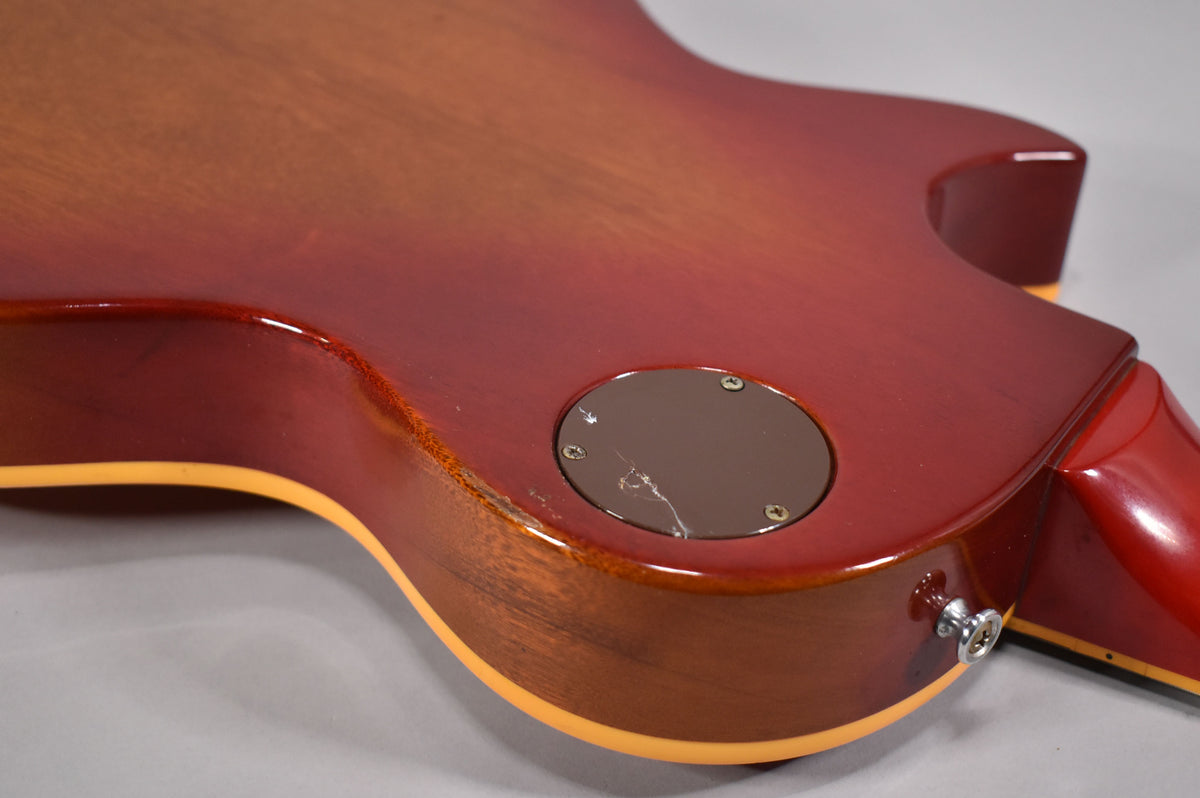 The lower back of a cherry sunburst guitar shows a cracked control cavity cover and wear on the binding and body edge.