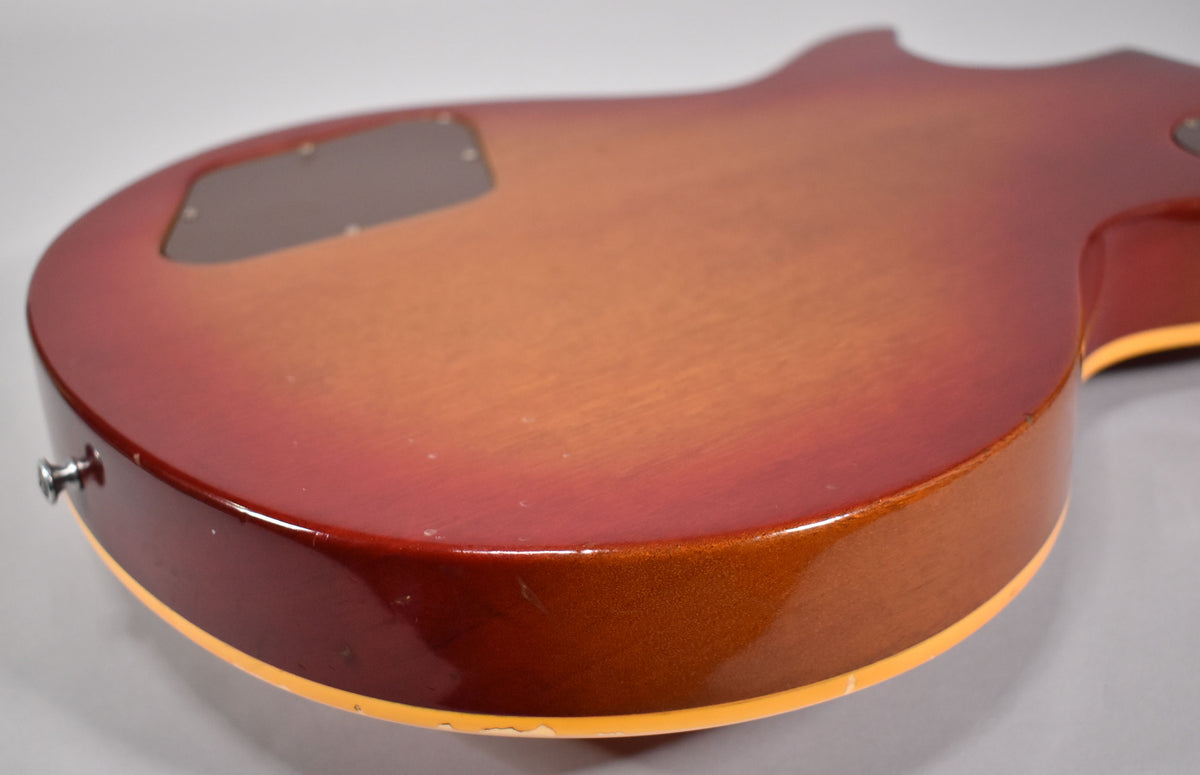 The guitar's cherry sunburst back shows a dark control cavity cover, a chrome strap button, and some finish wear along the binding.