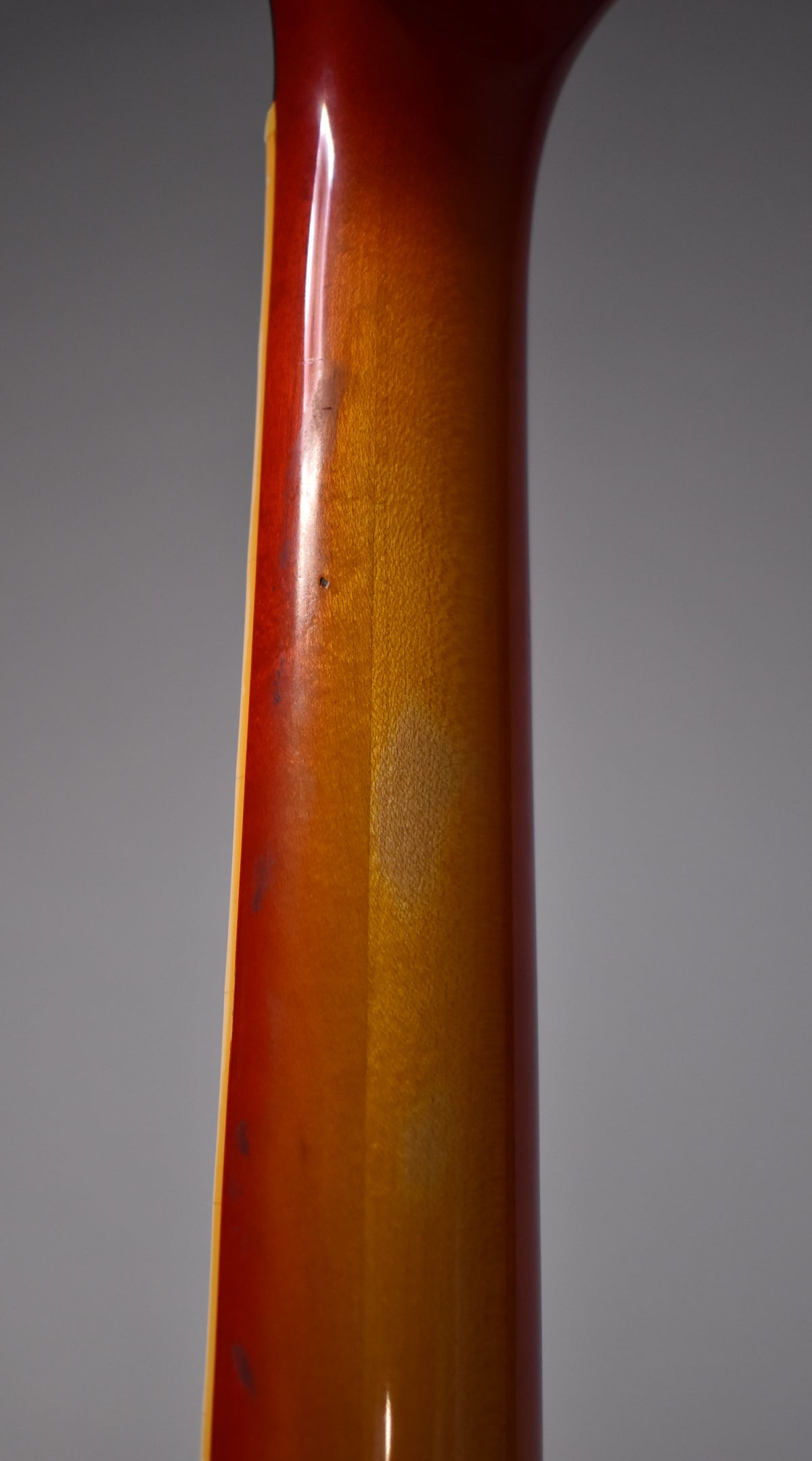 The guitar's cherry sunburst neck, viewed from the back, shows a glossy finish with some minor scuffs and wear marks.