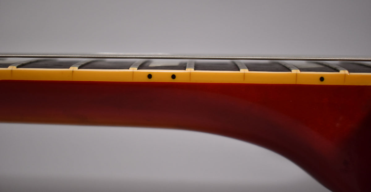 Close-up of the guitar's neck from the side, showing the dark fretboard, cream binding with black dot markers, and cherry sunburst finish.