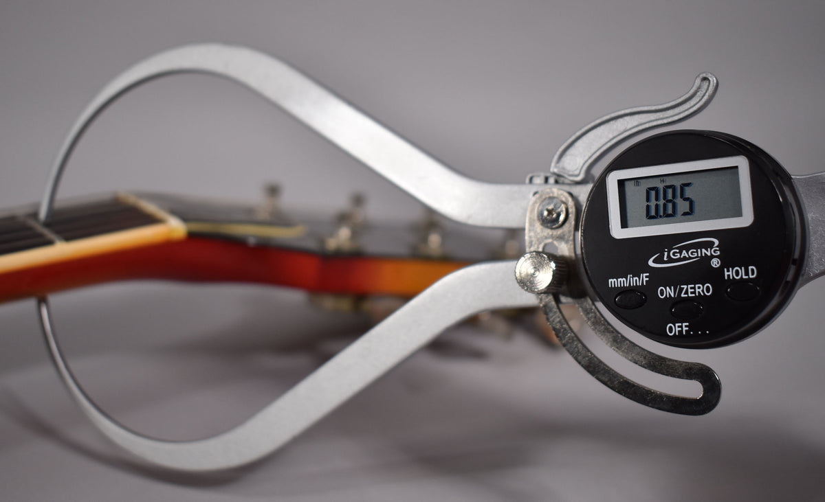 A digital caliper measures the neck thickness of the cherry sunburst guitar, showing 0.85 on its display.
