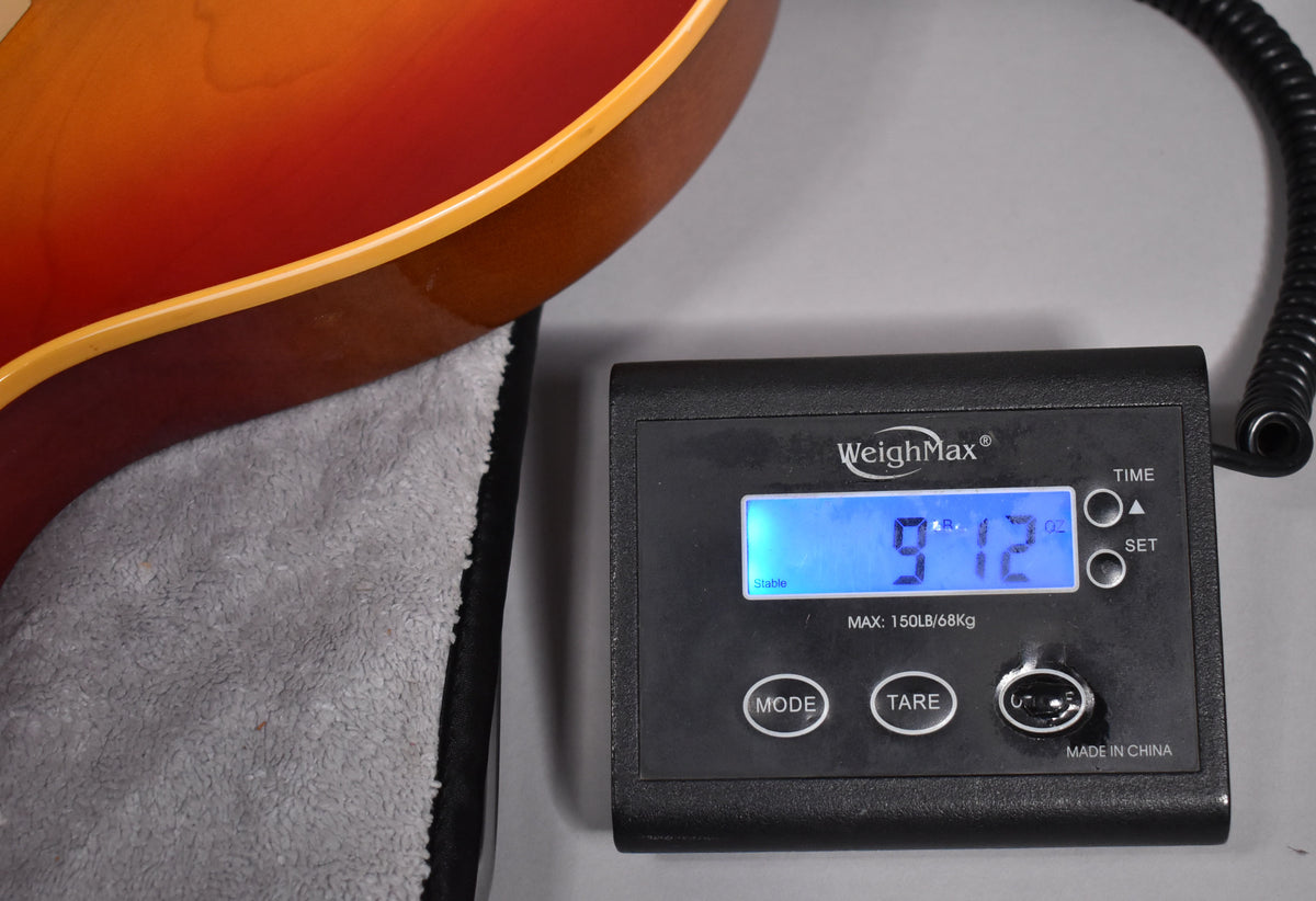 The guitar's cherry sunburst body is partially visible, resting on a grey cloth next to a digital scale displaying "9.12" lbs.