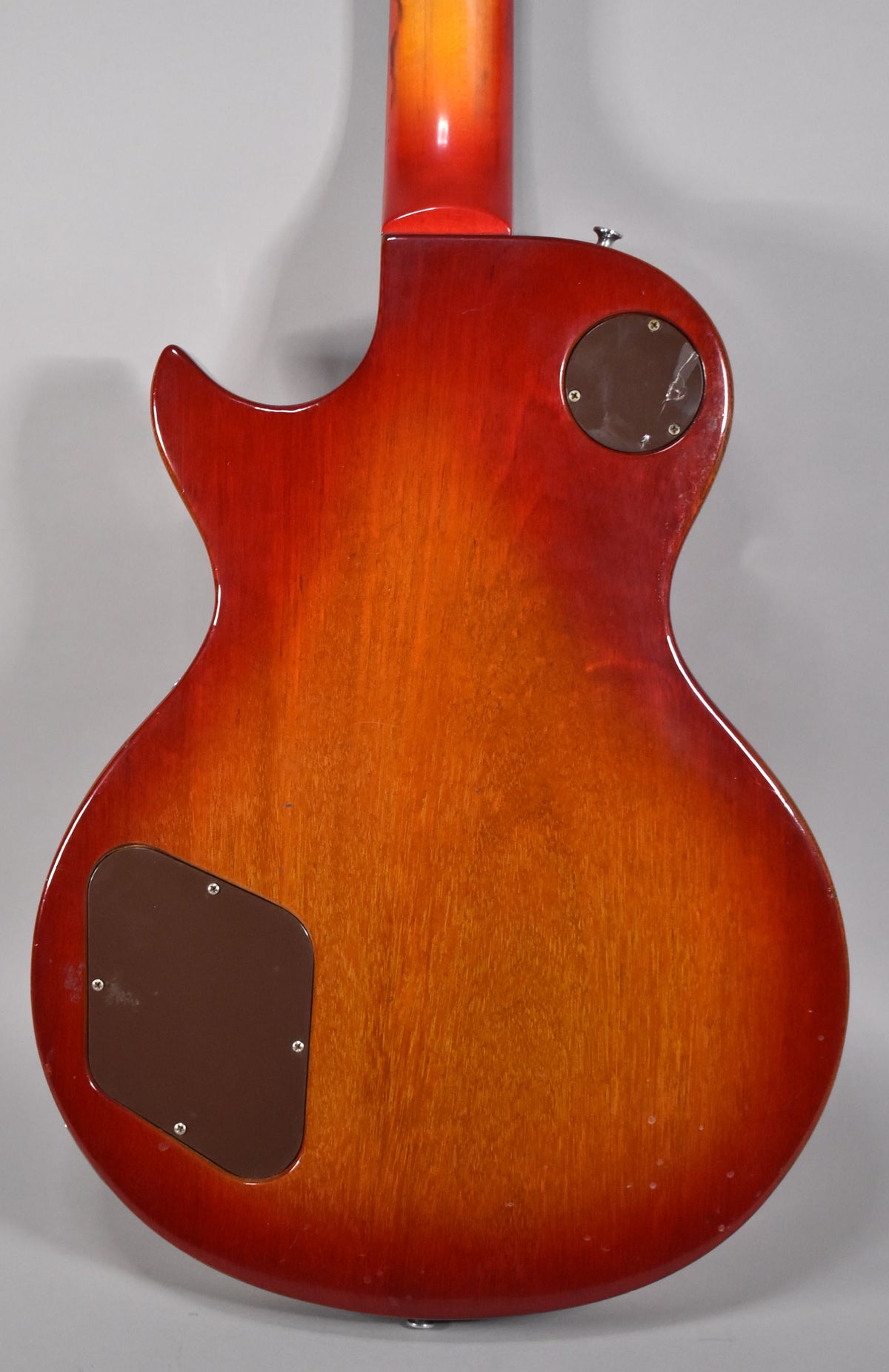 The back of a cherry sunburst electric guitar, showing the neck joint, two brown control cavity covers, and some minor dings.