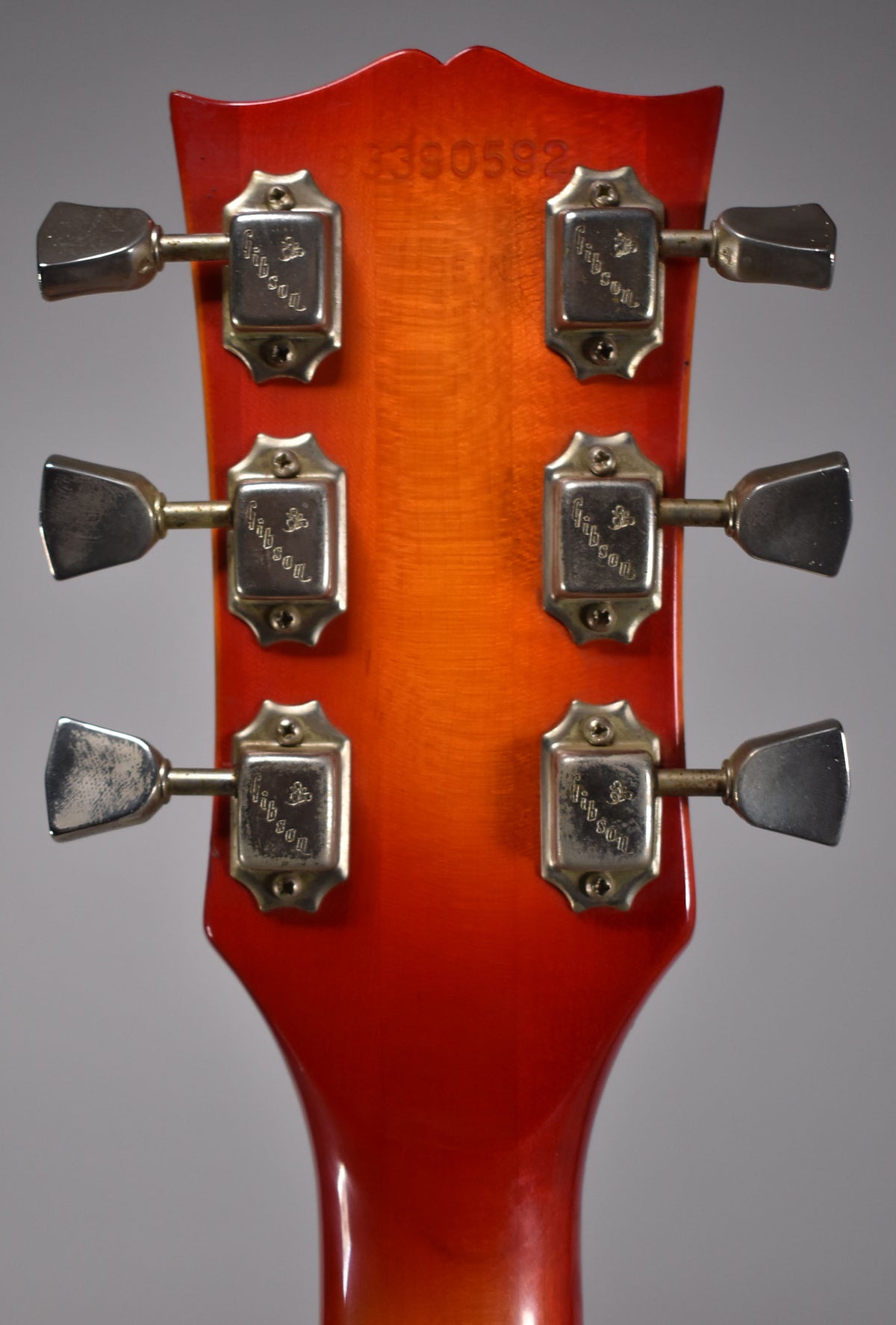 The back of a cherry sunburst headstock with six tarnished chrome tuners, three on each side, and a faint serial number.
