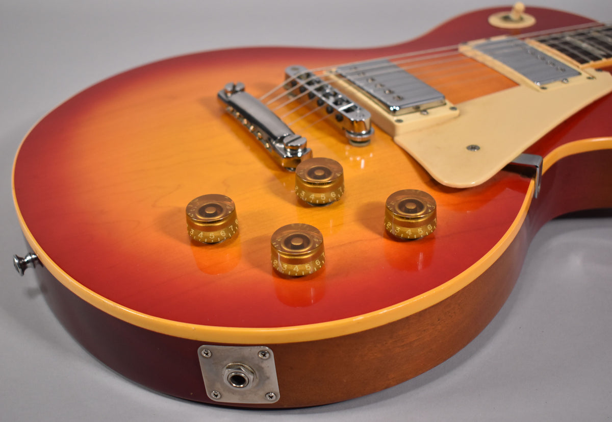 Close-up of the lower body, showing the cherry sunburst finish, four gold top hat knobs, chrome bridge, and cream pickguard.