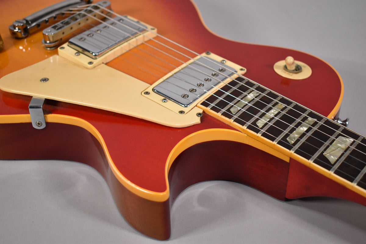Upper body of a cherry sunburst guitar, showing the cream pickguard, two chrome humbuckers, and trapezoid fretboard inlays.