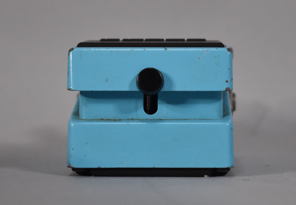 The light blue pedal is seen from the right side, showing a black thumbscrew and visible chips and scratches on the finish.