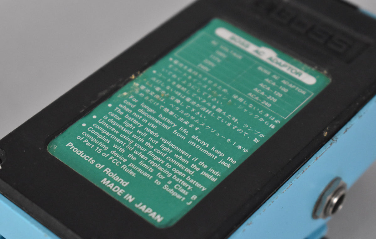A close-up of the pedal's light blue side and black base, showing a green label with white text and some paint chips.