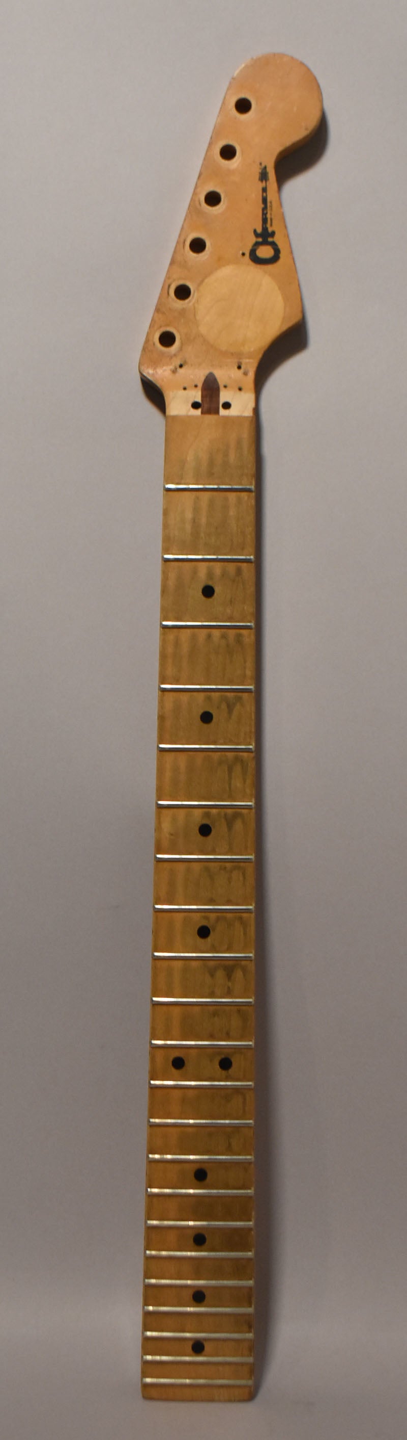 A full-length view of a light maple neck with a Strat-style headstock, showing dark fret markers and some wear on the fretboard.
