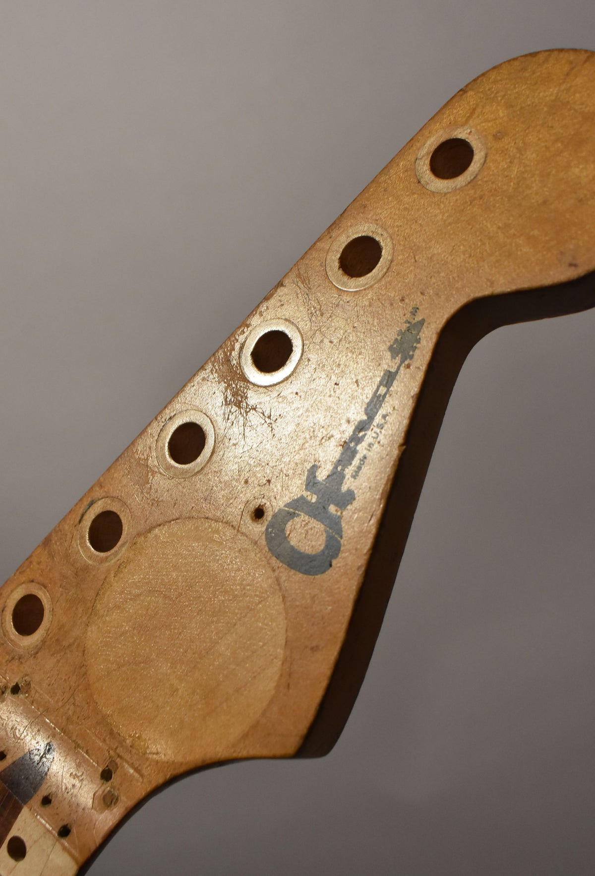 Close-up of a maple headstock with six tuner holes, a dark logo, and heavy finish checking and wear, viewed from the top right.