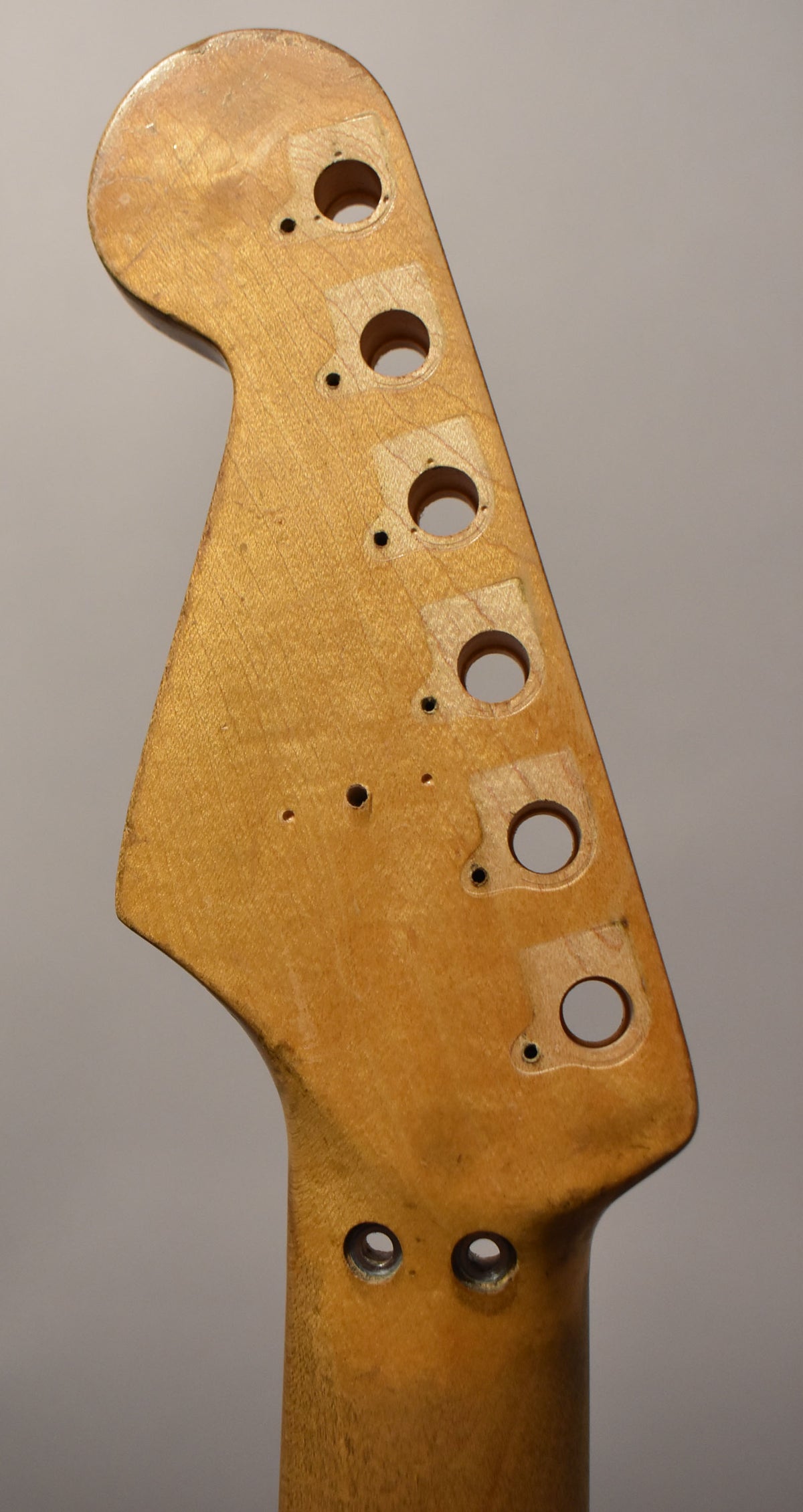 Close-up of a worn, light maple headstock with six tuner holes, two neck mounting holes, and several small pilot holes.