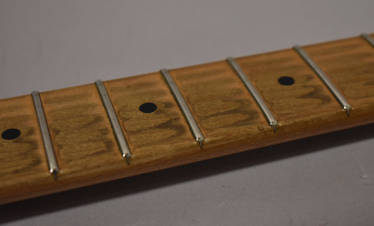 Close-up of a maple fretboard with dark circular inlays and silver frets, showing some dark discoloration and wear on the wood.