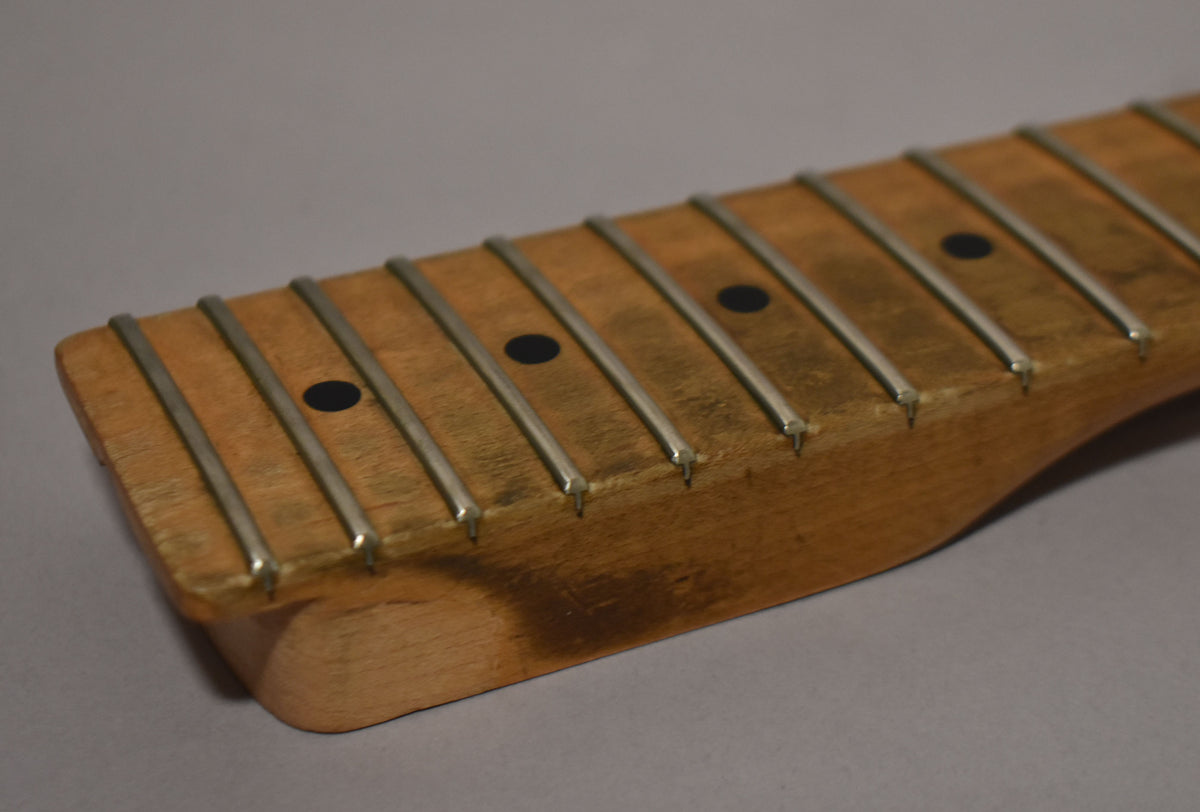 Close-up of a maple fretboard with dark circular inlays, showing wear and discoloration on the wood and tarnished frets.