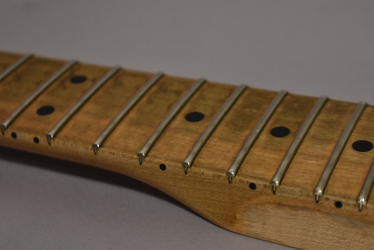 Close-up of the maple fretboard, showing dark dot inlays, worn frets, and visible wear around the fret ends.