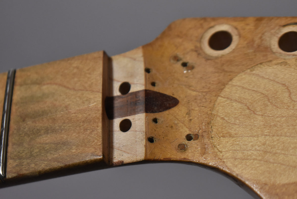 Close-up of the maple headstock and nut, showing two tuner holes, several small screw holes, and a dark wood string tree.