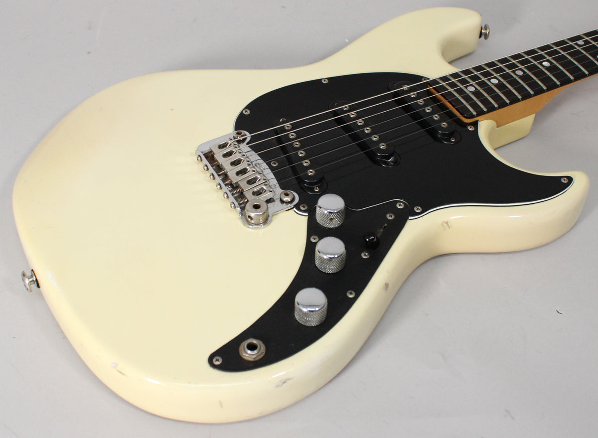 Upper body of an Olympic White electric guitar with a black pickguard, three chrome knobs, and a chrome tremolo bridge.