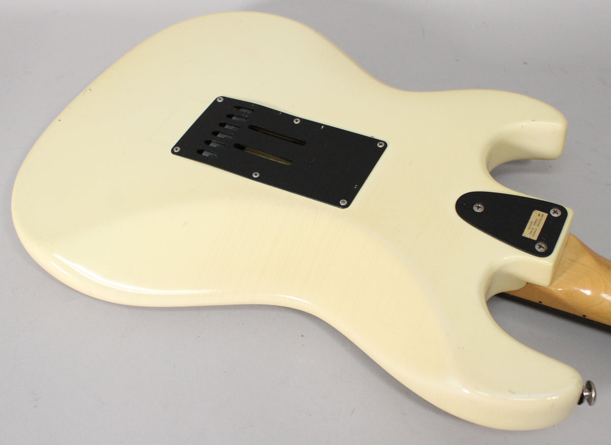 The back of an Olympic White electric guitar body, showing a black tremolo cavity cover and a smaller black control plate.