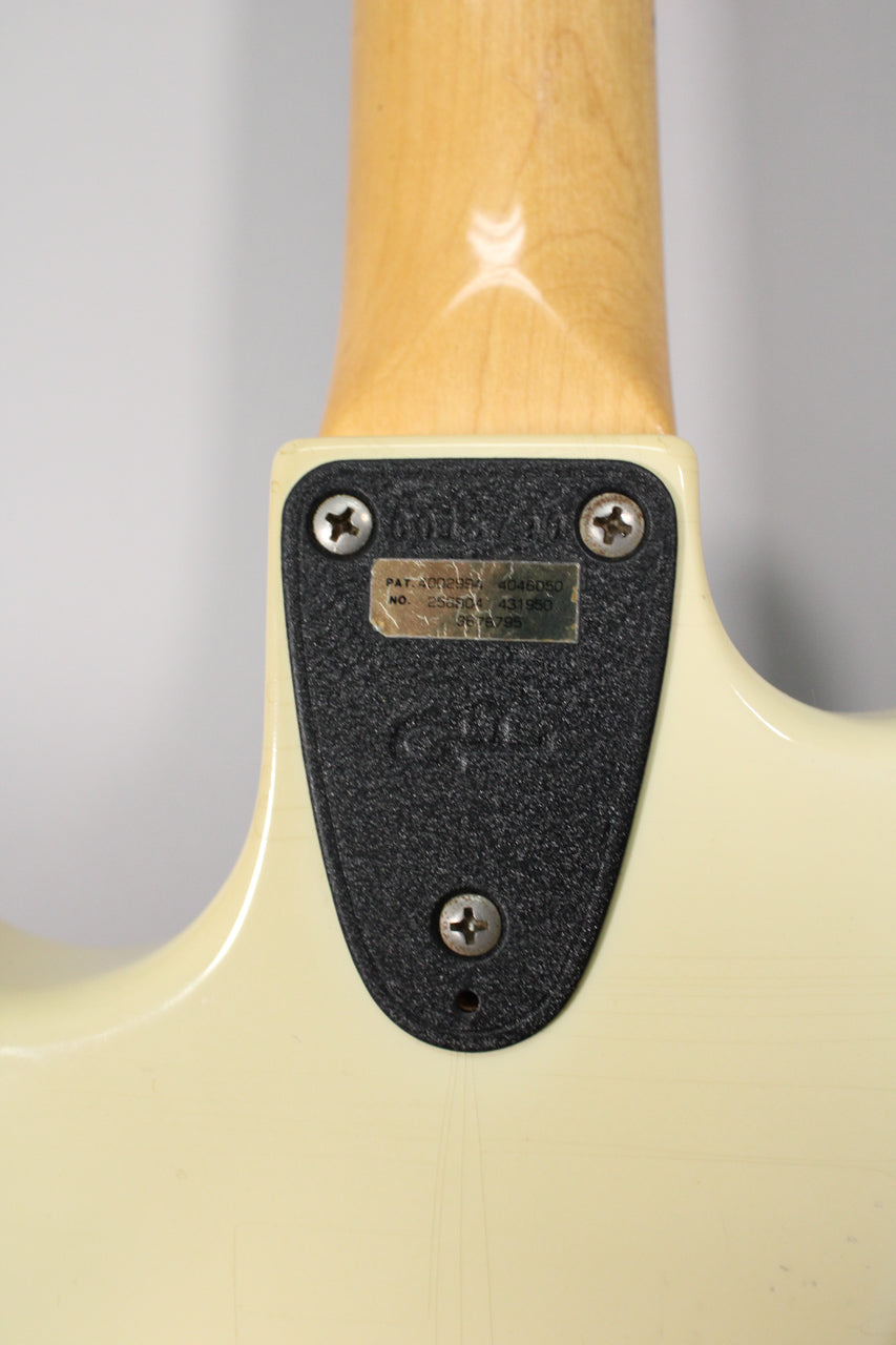 The guitar's Olympic White body shows fine finish checking around the neck plate, which has a black textured pad and patent numbers.