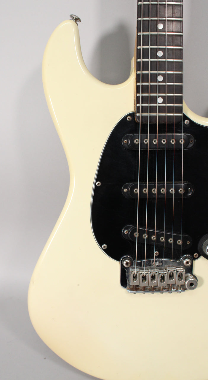 Upper body of an Olympic White guitar with a black pickguard, three single-coil pickups, and a chrome tremolo bridge.