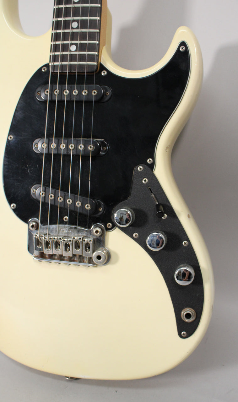 Close-up of the Olympic White body and black pickguard, showing two humbuckers, a tremolo bridge, three chrome knobs, and a toggle switch.