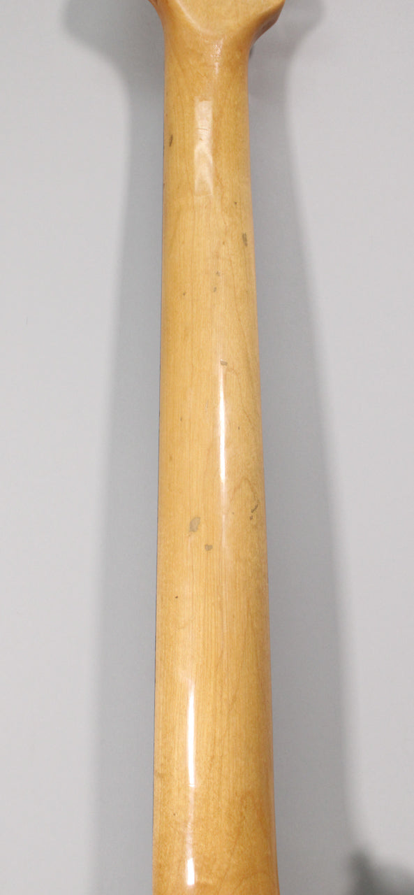 The back of a light maple guitar neck, showing several small dark dings and a glossy finish, tapering slightly at the top.