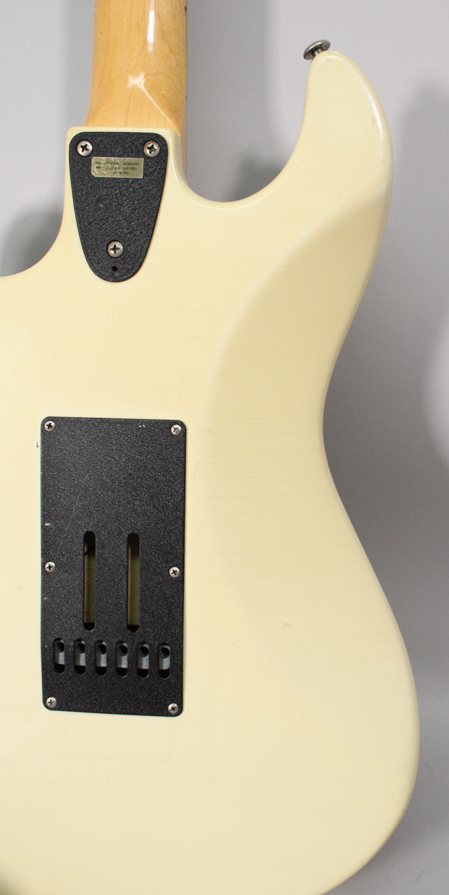 The back of an Olympic White guitar body, showing the neck joint, black tremolo cavity cover, and a strap button.