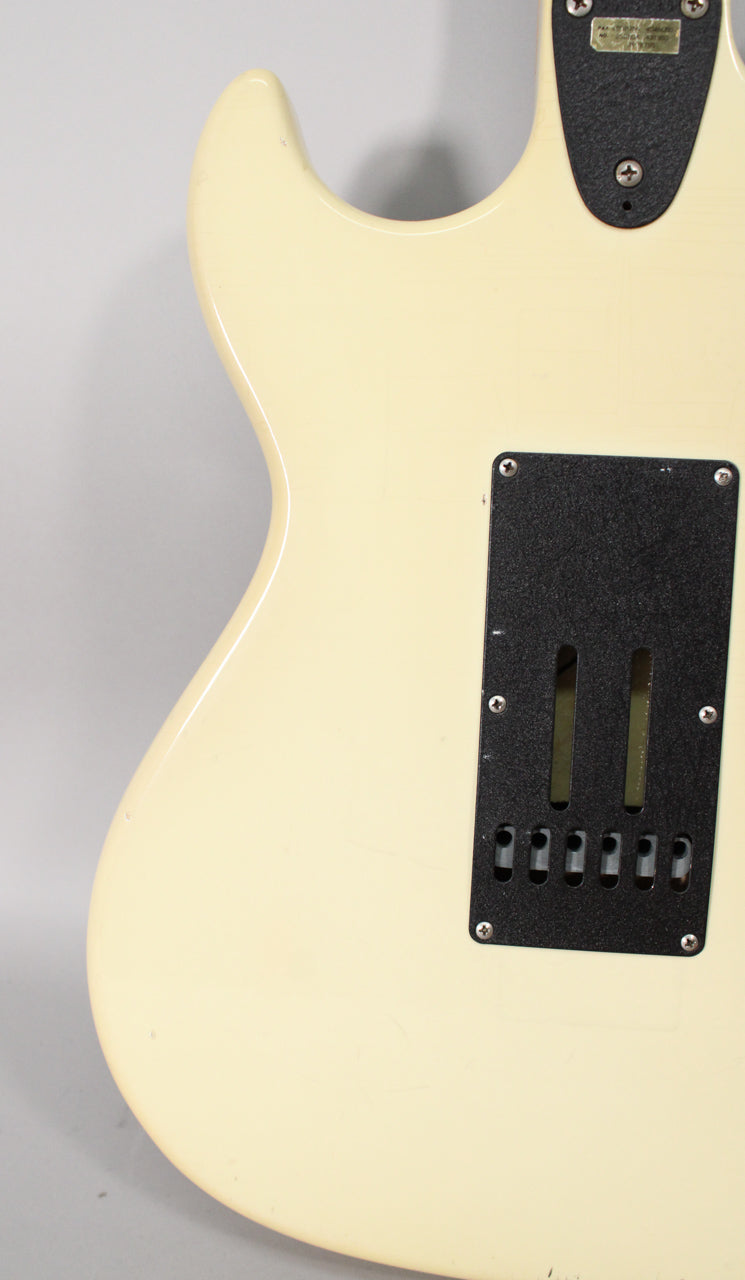 The back of an Olympic White guitar body, showing the black tremolo cavity cover and neck plate, with minor scuffs.
