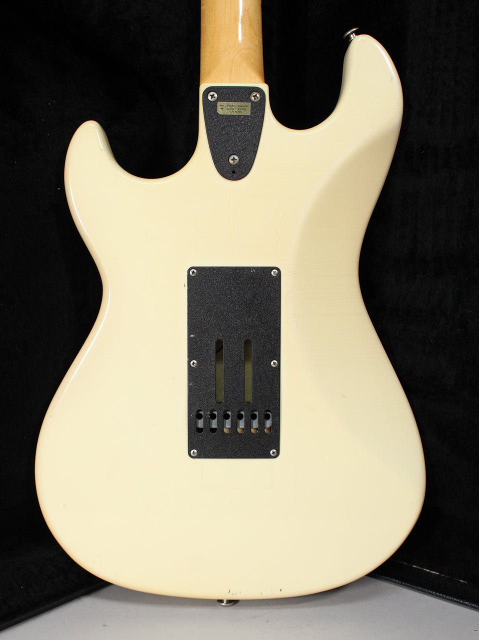 The back of an Olympic White guitar shows a black tremolo cavity cover, a neck plate, and light wear on the lower bout.