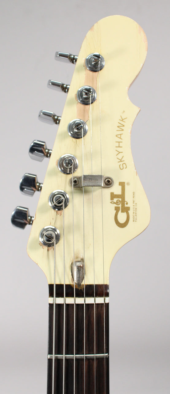 Close-up of the guitar's cream headstock, showing six chrome tuners, a string tree, and significant finish wear around the tuning pegs.