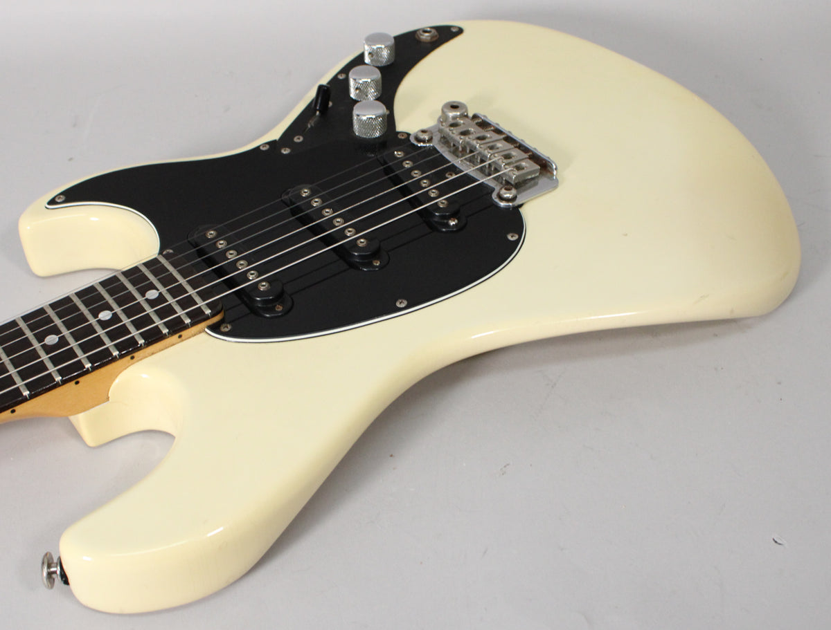 Olympic white guitar body, black pickguard, three pickups, chrome bridge, and three knurled chrome knobs.