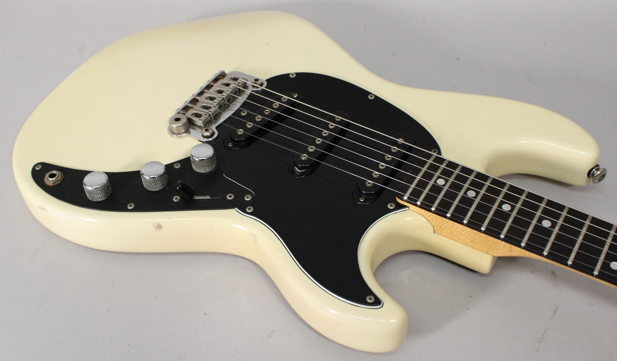 Olympic white electric guitar, angled view of the body, black pickguard, three single-coil pickups, and chrome hardware.