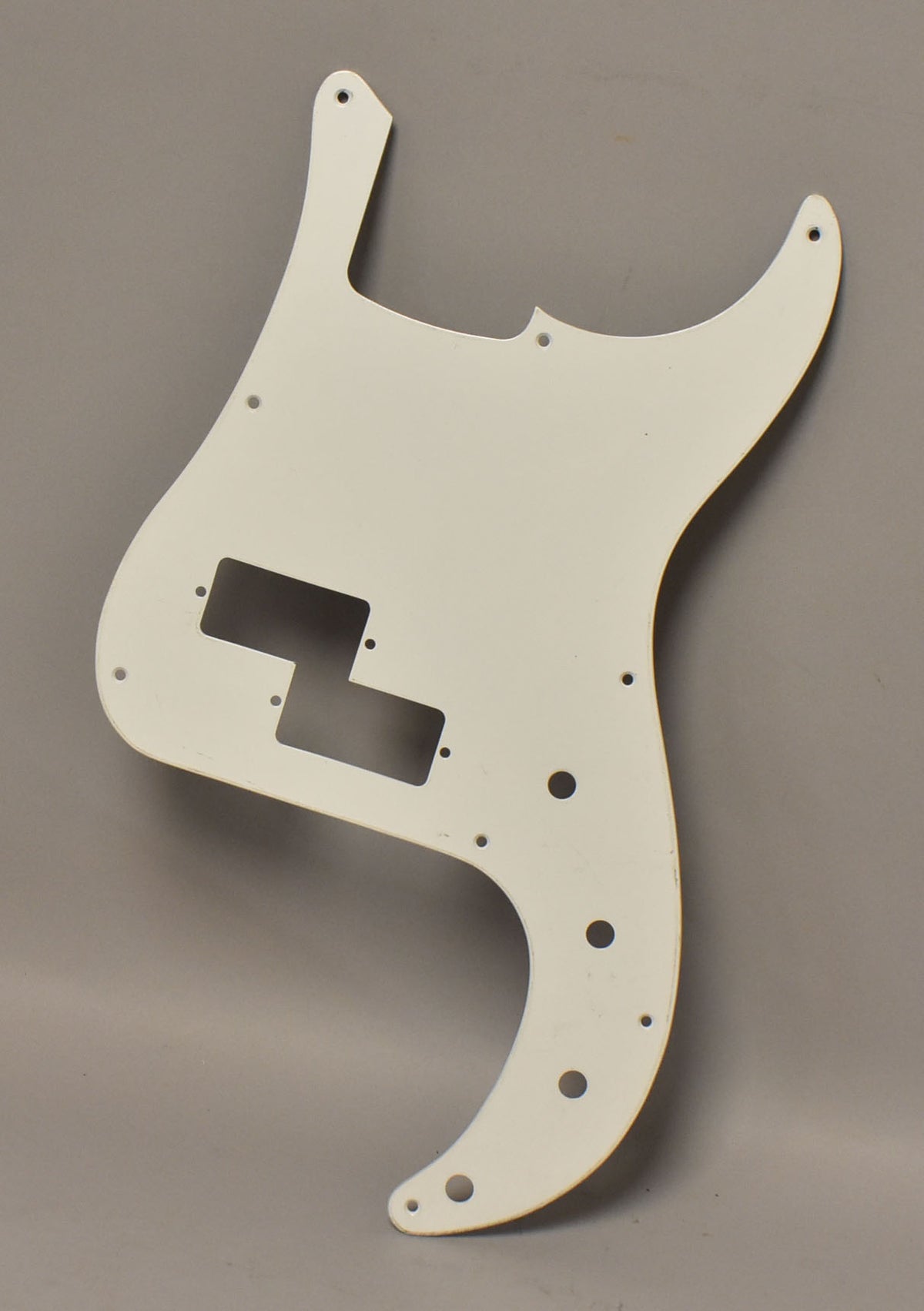 White coated aluminum P-style bass pickguard, viewed from above, with a split pickup cutout and ten screw holes.