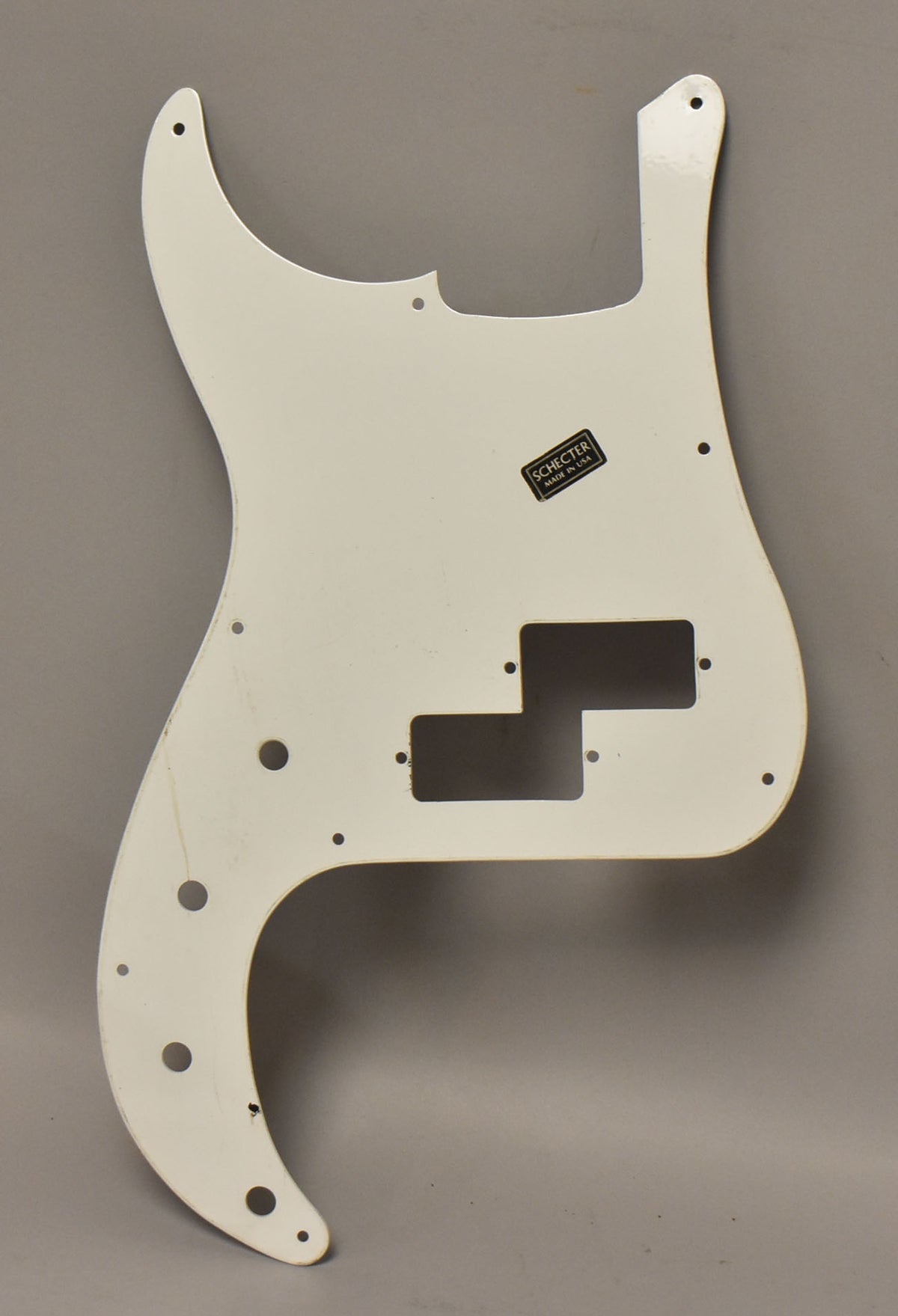 White coated aluminum P-style bass pickguard, viewed from above, showing a pickup cutout and screw holes.