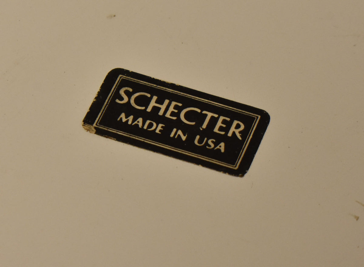 Close-up of the pickguard's top right corner, showing a black "Schecter Made in USA" sticker with minor edge wear.